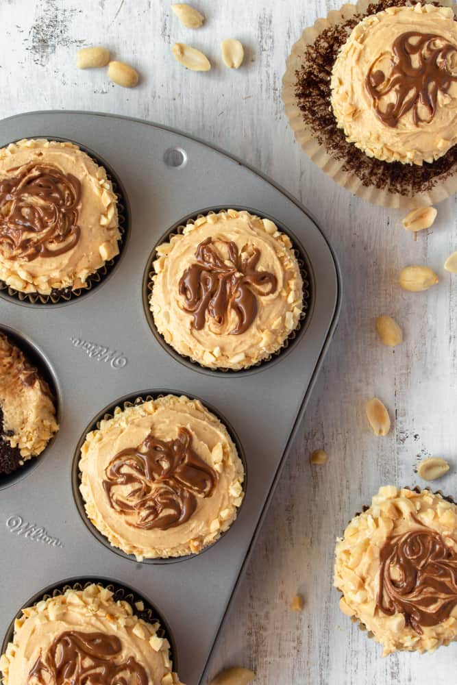 Peanut butter cupcakes with a chocolate swirl in a muffin tin.