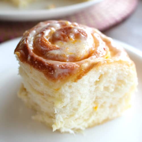 A square hero shot of a fluffy lemon roll on a white plate.