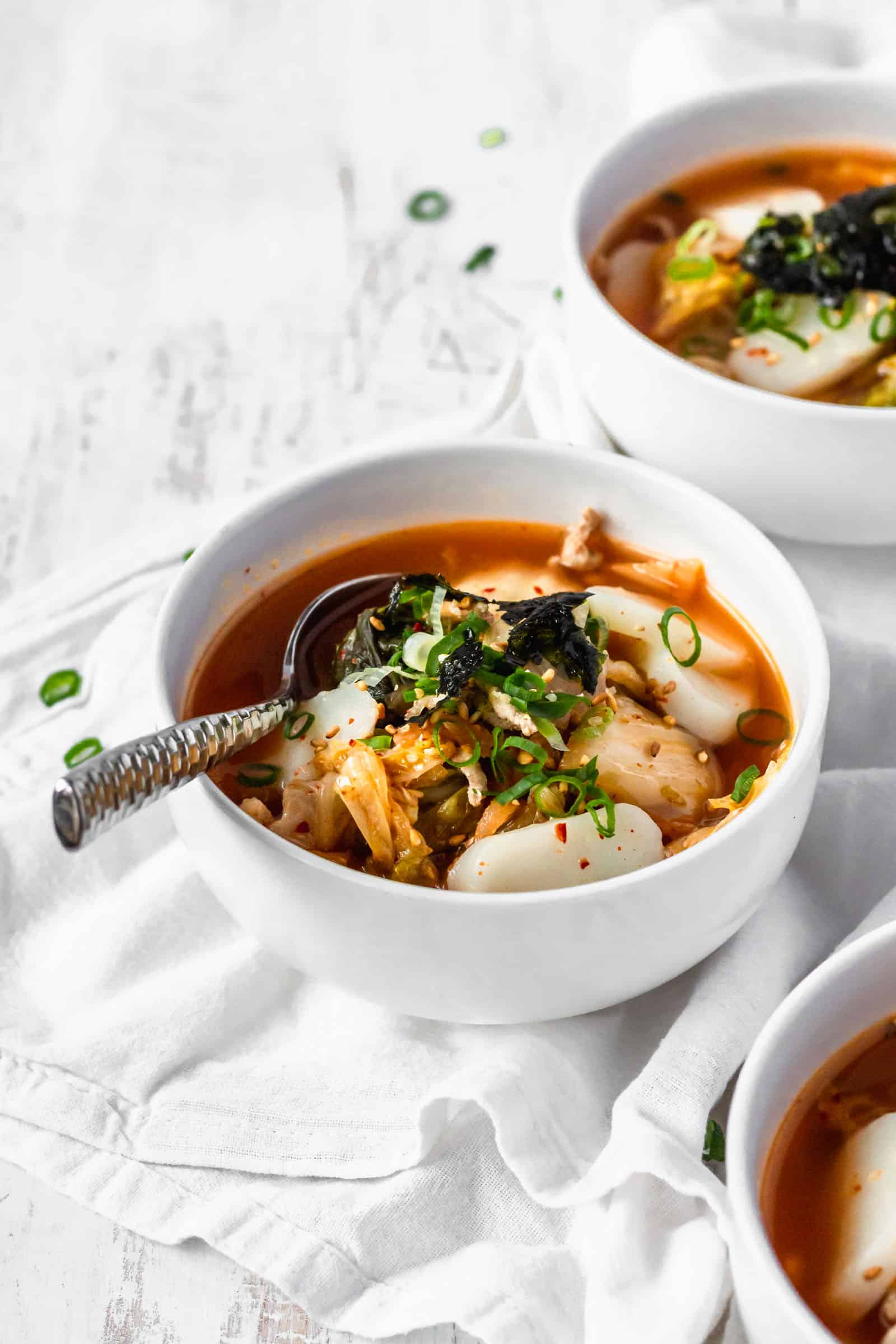Three bowls of Korean rice cake soup with kimchi with a spoon in the bowl.