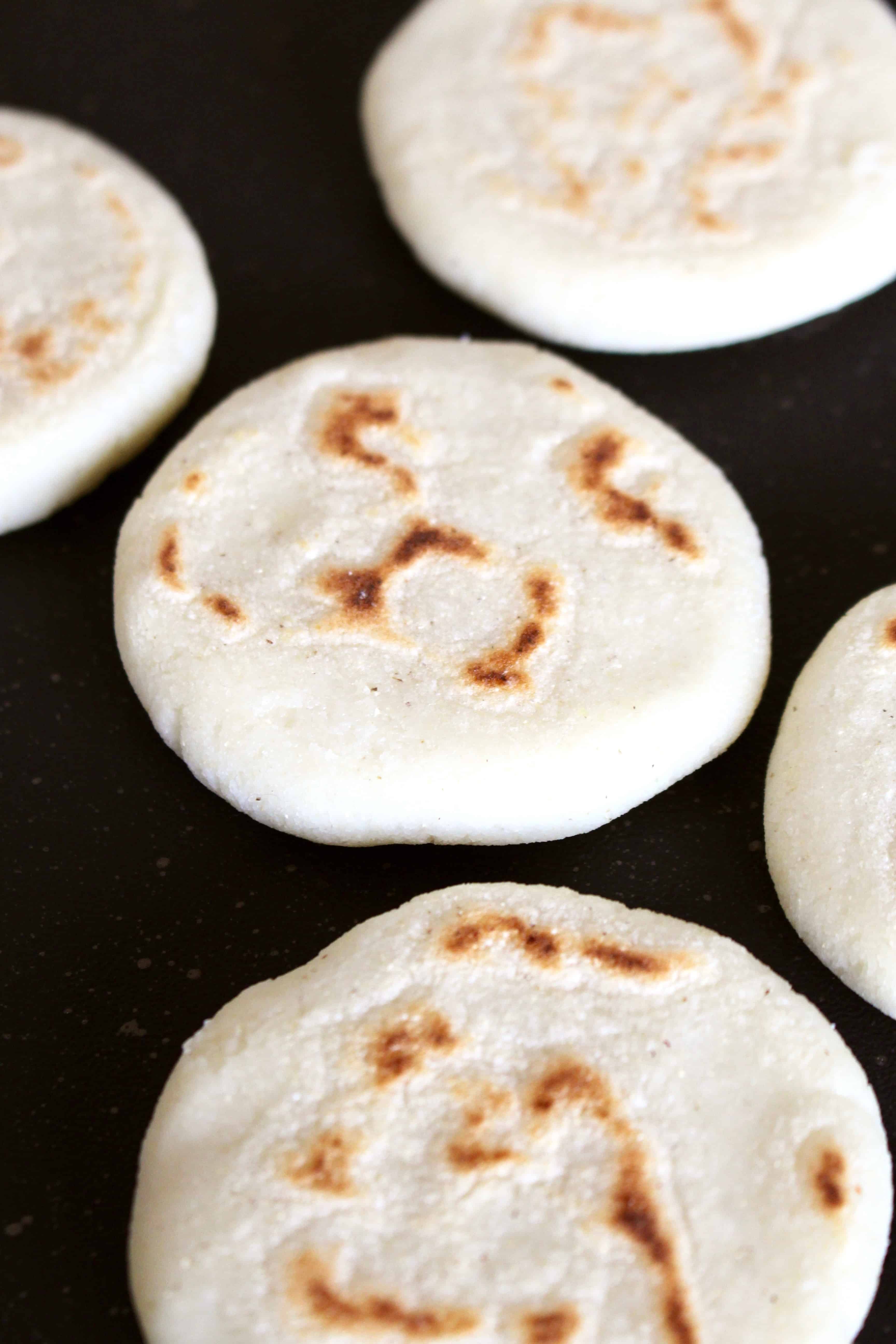 Arepas cooking on a dark metal pan.
