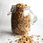 A glass jar of gluten-free granola on a white surface with some spilled out.