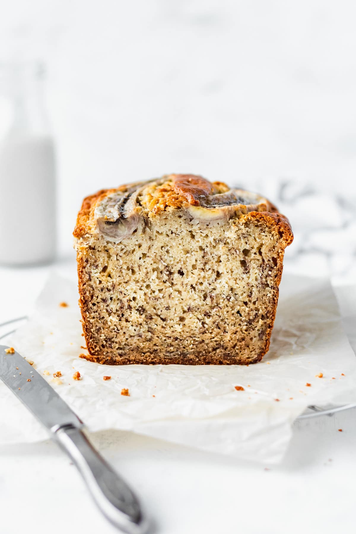 A sliced loaf of moist banana bread with a knife next to it.