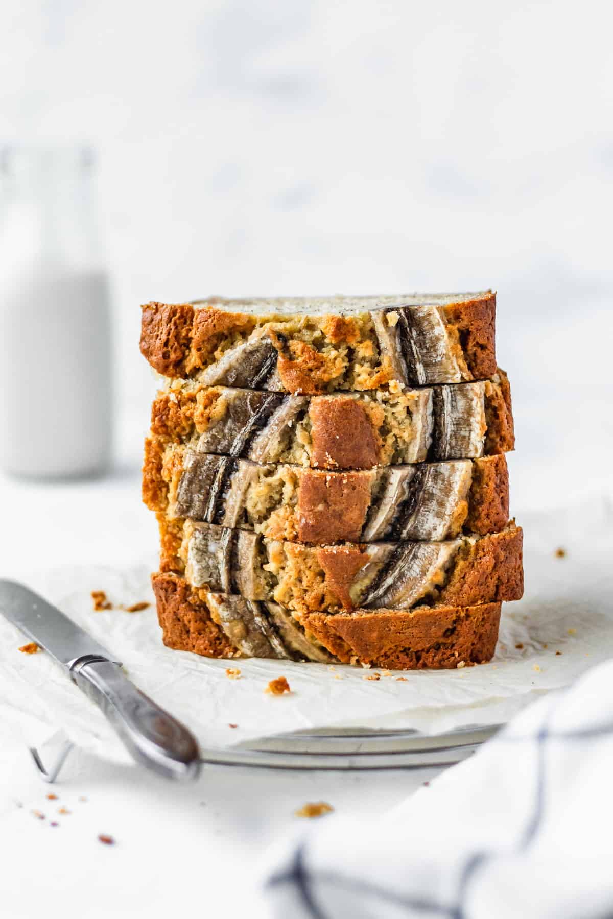 A stack of moist banana bread on parchment paper with a bottle of milk in the background.