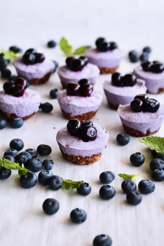Blueberry cheesecake bites scattered on a white surface with mint leaves and fresh blueberries.