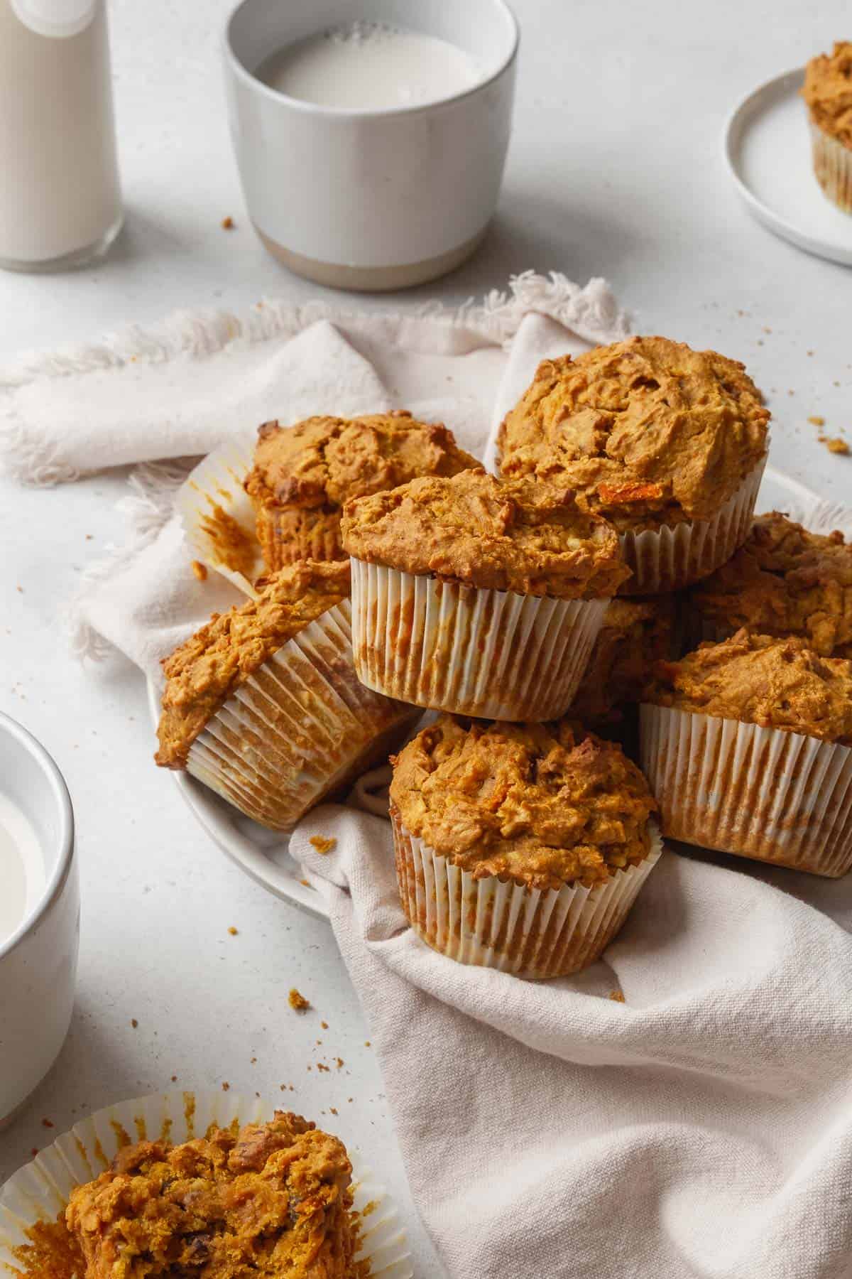 45 degree hero shot of a pile of healthy vegan morning glory muffins on a white table with a glass of vegan milk in the background.