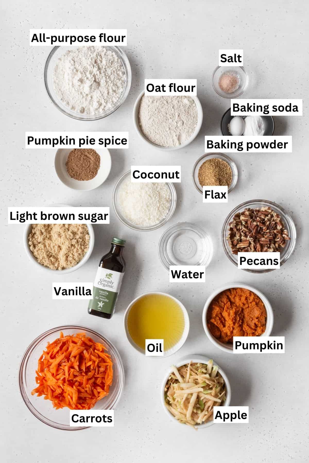 Ingredients needed to make healthy pumpkin morning glory muffins measured out into bowls on a white table with text overlay.