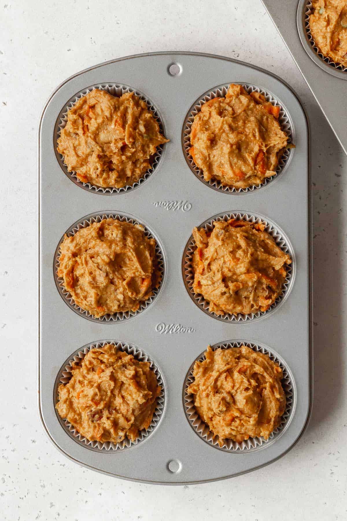 Process shot - 6 cup muffin tin filled with muffin tin liners filled with morning glory muffin batter.