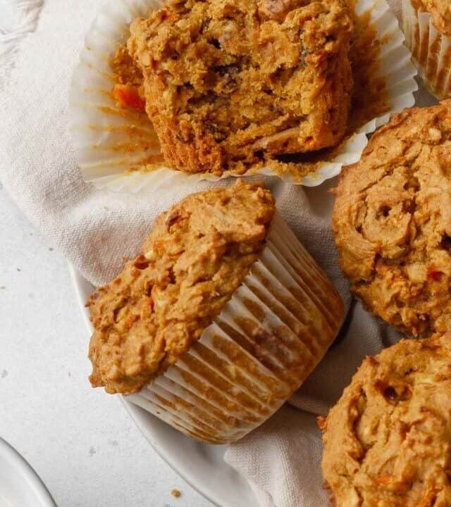 overhead shot of morning glory muffins with one that has a bite taken out and turned on its side so you can see the moist interior.
