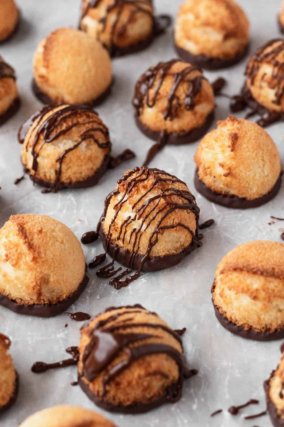 Plain and chocolate drizzled vegan coconut macaroons on a white surface.
