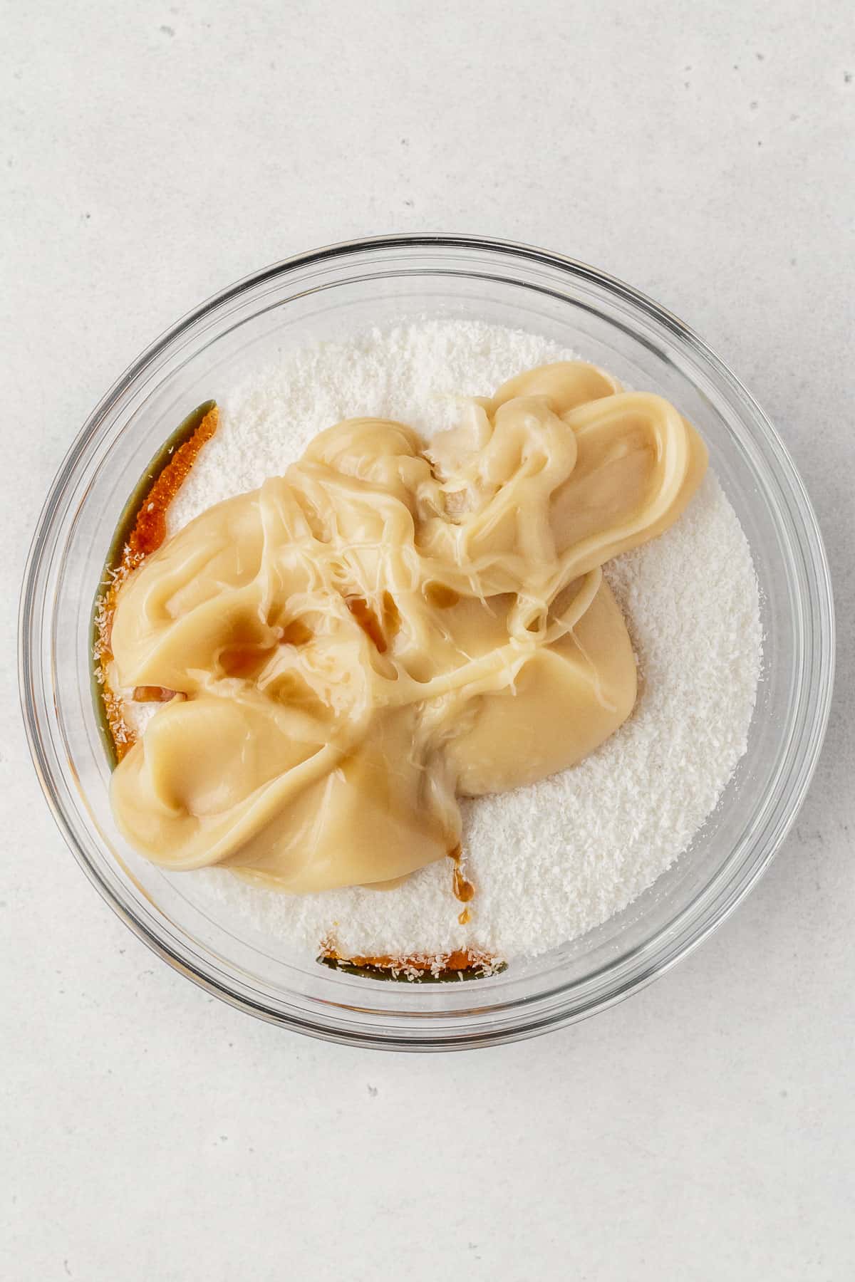Coconut, vegan condensed milk, and vanilla extract in a glass bowl.