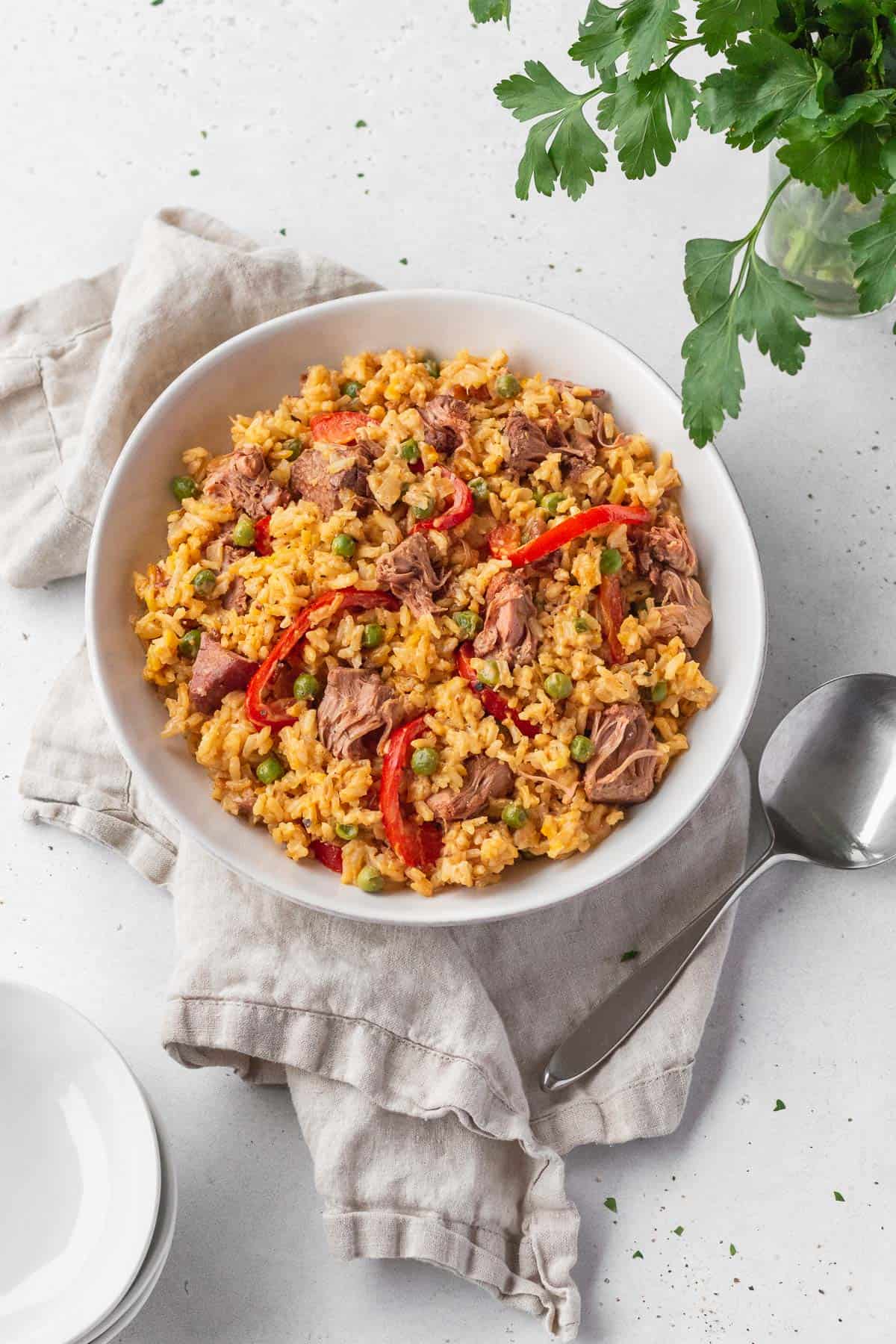 Overhead shot of vegan Arroz Valenciana in a white bowl with a spoon and natural linen.
