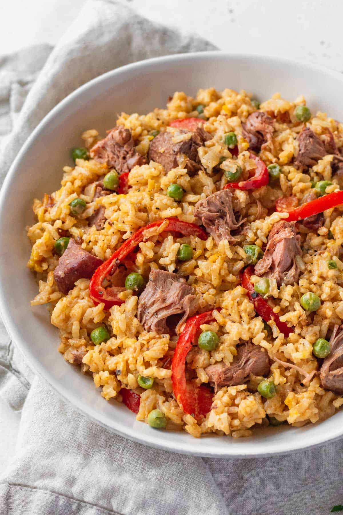 A big bowl of vegan Filipino rice with sliced red bell peppers and peas.