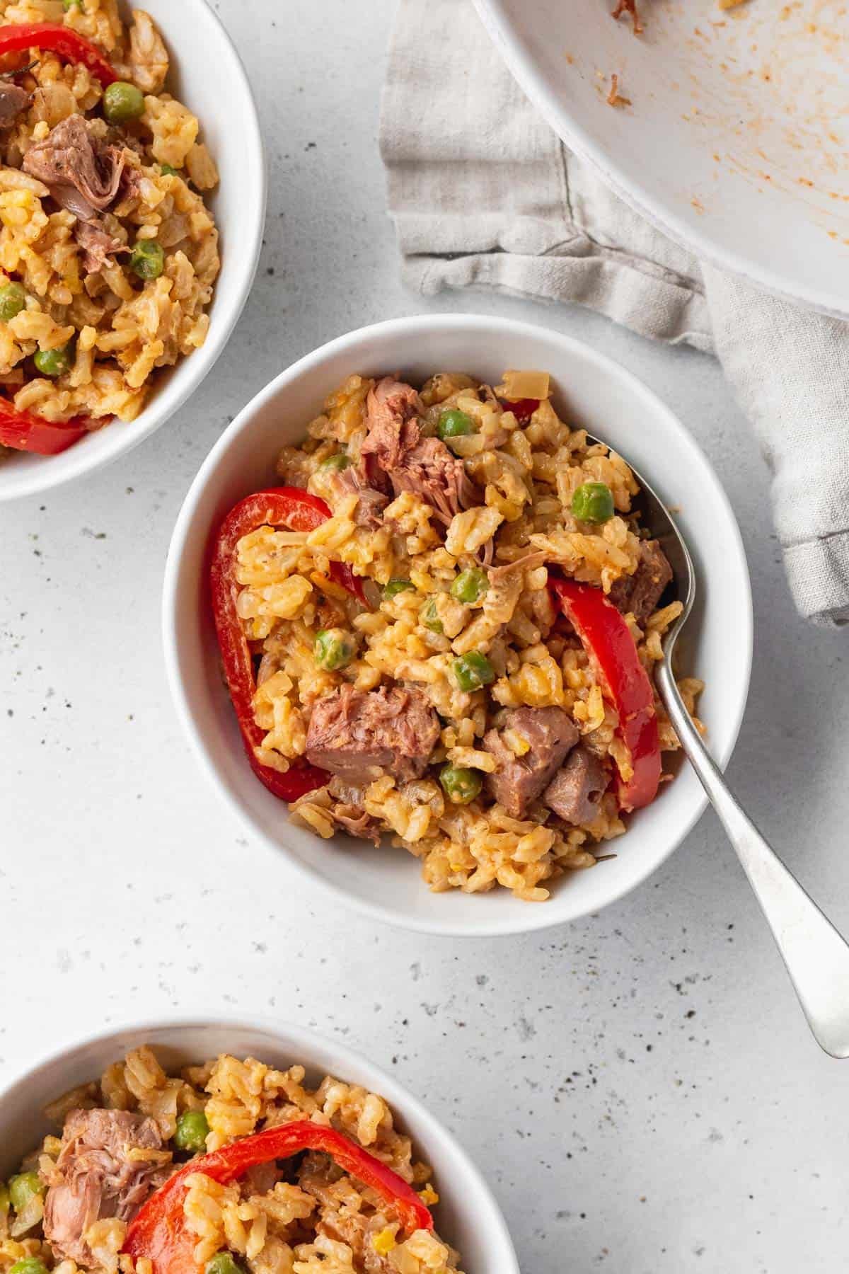 Valencian style rice in a bowl with a silver spoon, with 2 more bowls in the corners of the shot.