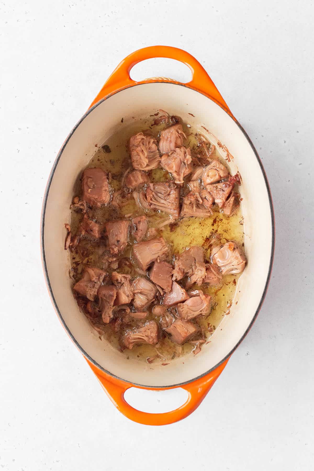 Young green jackfruit confit being cooked in oil in a pot.
