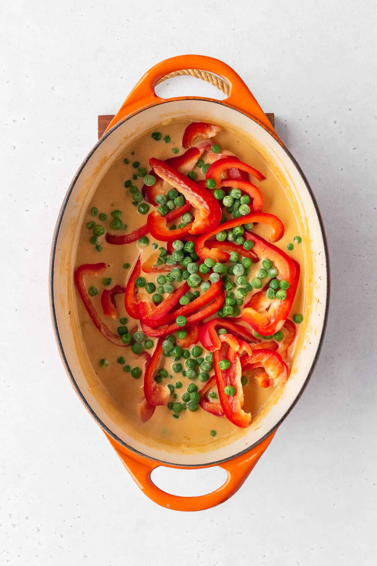 Frozen peas and sliced red bell peppers added to the pot.