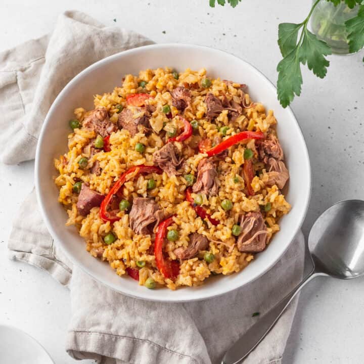 Overhead shot of vegan Arroz Valenciana in a white bowl with a spoon and natural linen.