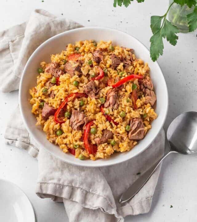 Overhead shot of vegan Arroz Valenciana in a white bowl with a spoon and natural linen.