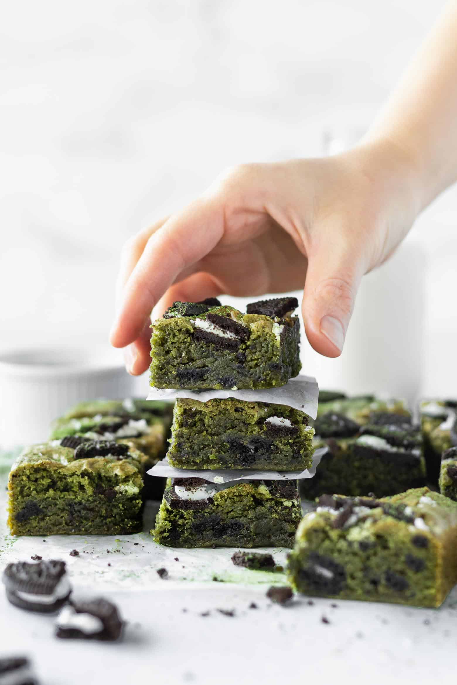 A hand reaching for a stack of matcha blondies