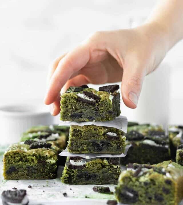 A hand reaching for a stack of matcha blondies