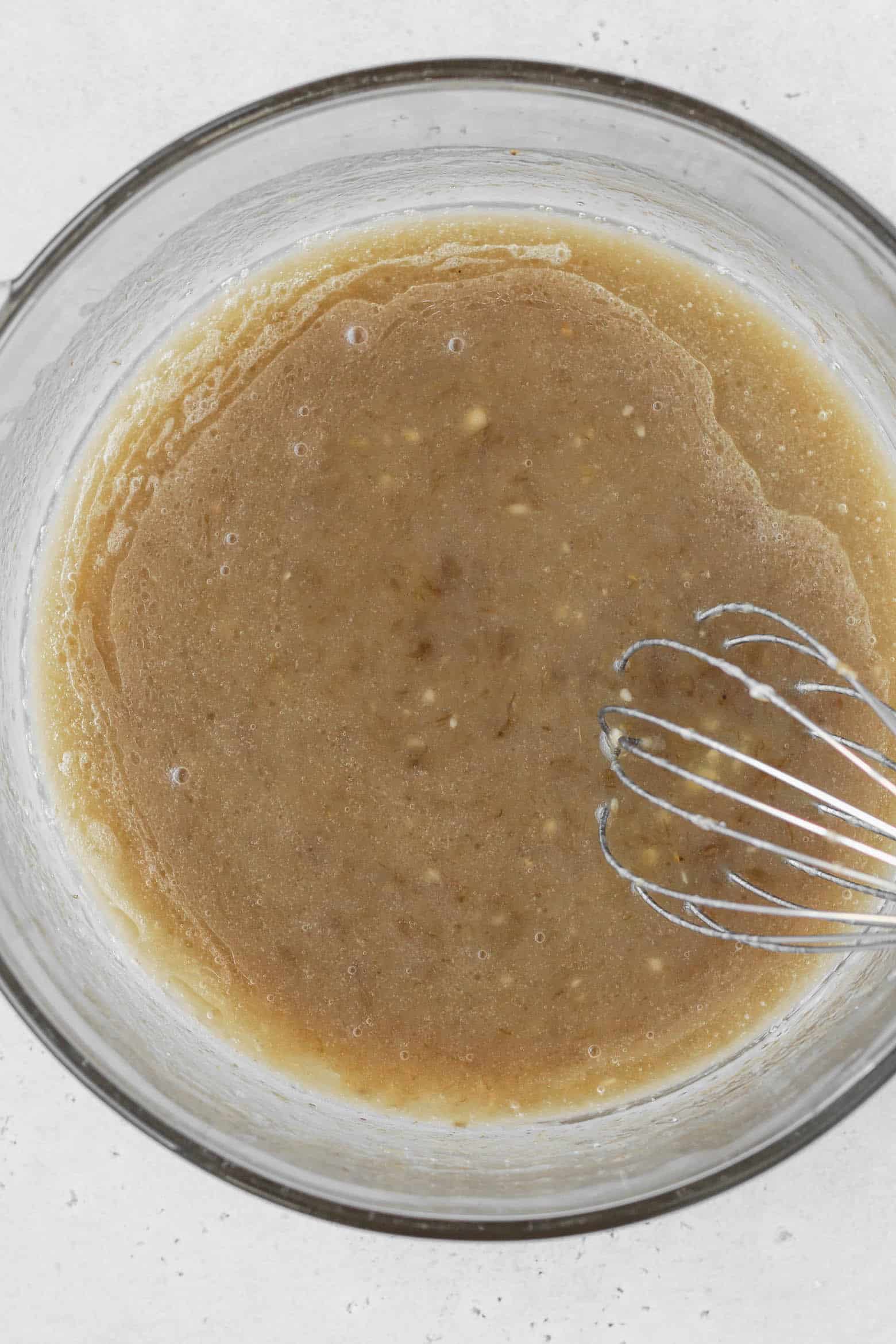 A bowl of oil, mashed banana, sugar, and vanilla extract mixed together.