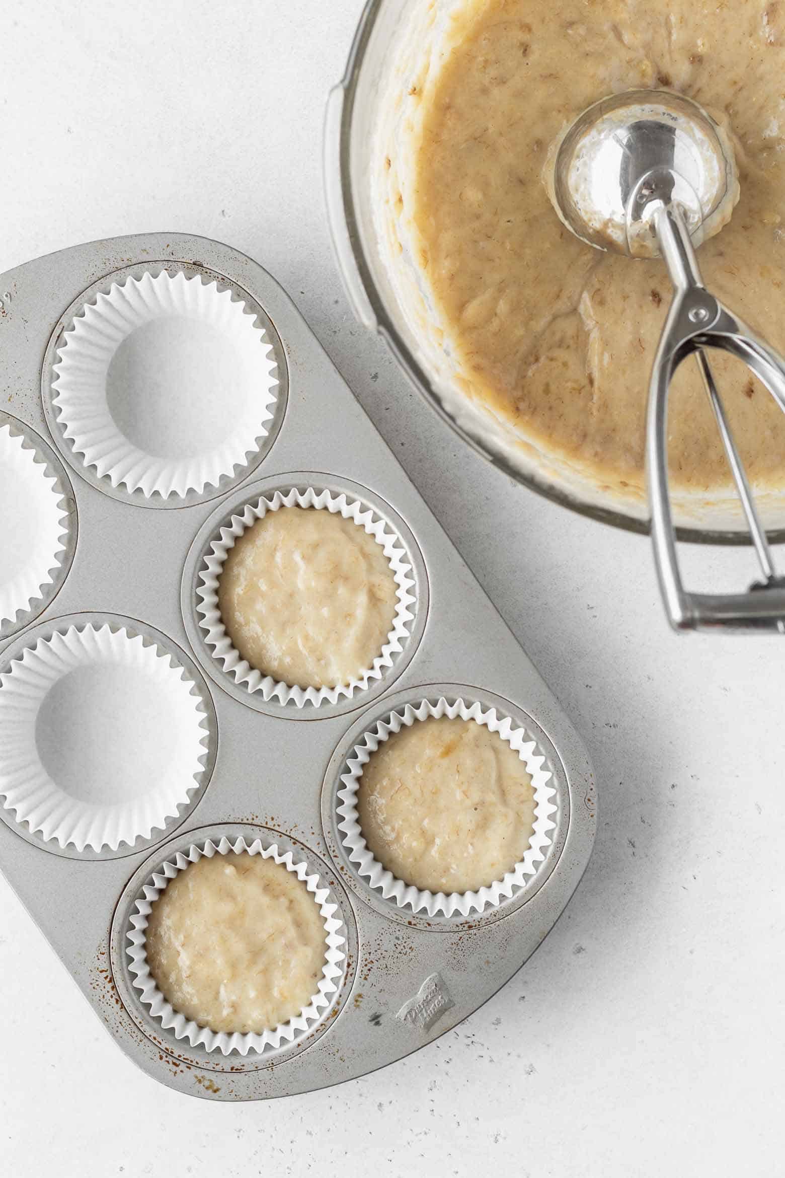 Vegan banana cupcake batter scooped into a cupcake pan using an ice cream scoop.