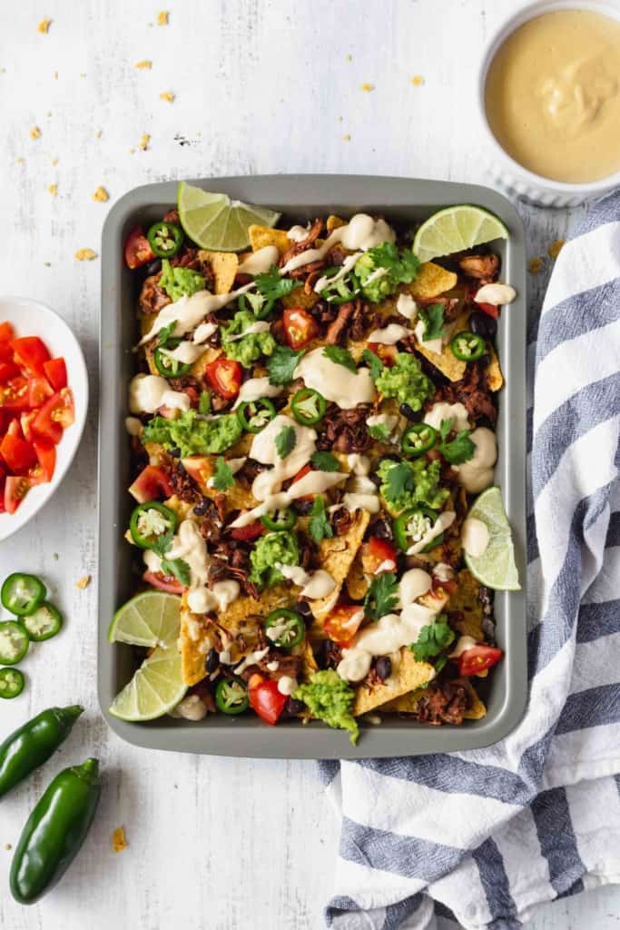Vegan nachos with jackfruit and vegan queso is amazing! Tortilla chips, jackfruit, black beans, tomatoes, guacamole, jalapeños, cilantro, and creamy queso! #vegannachos #vegancheese #veganqueso #jackfruit #veganmexicanfood