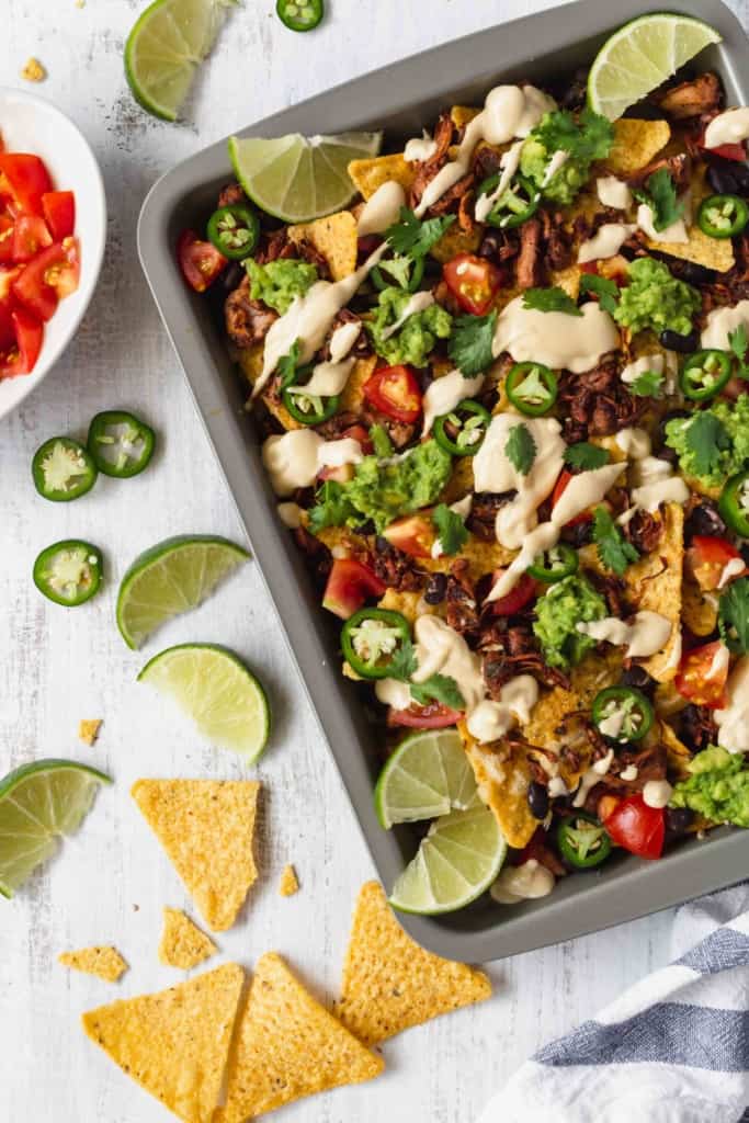 Vegan nachos with jackfruit and vegan queso is amazing! Tortilla chips, jackfruit, black beans, tomatoes, guacamole, jalapeños, cilantro, and creamy queso! #vegannachos #vegancheese #veganqueso #jackfruit #veganmexicanfood