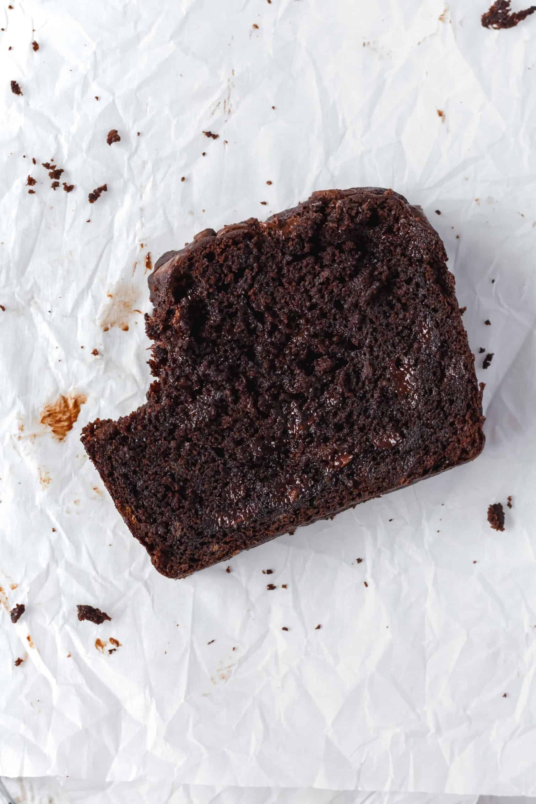 A slice of chocolate banana bread on a pice of parchment paper with a bite taken out.