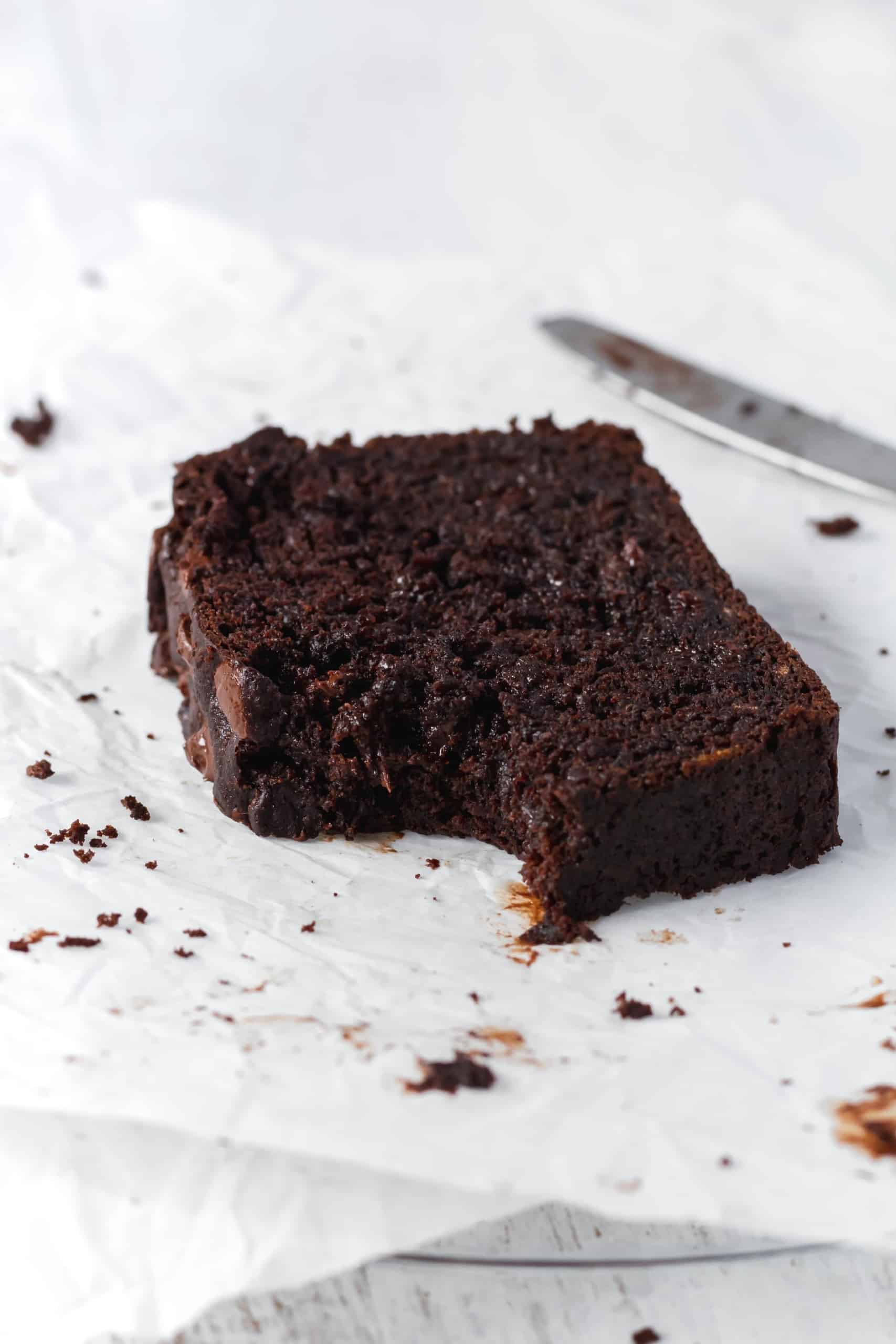 A bitten slice of moist chocolate banana bread on parchment paper with chocolate stains.