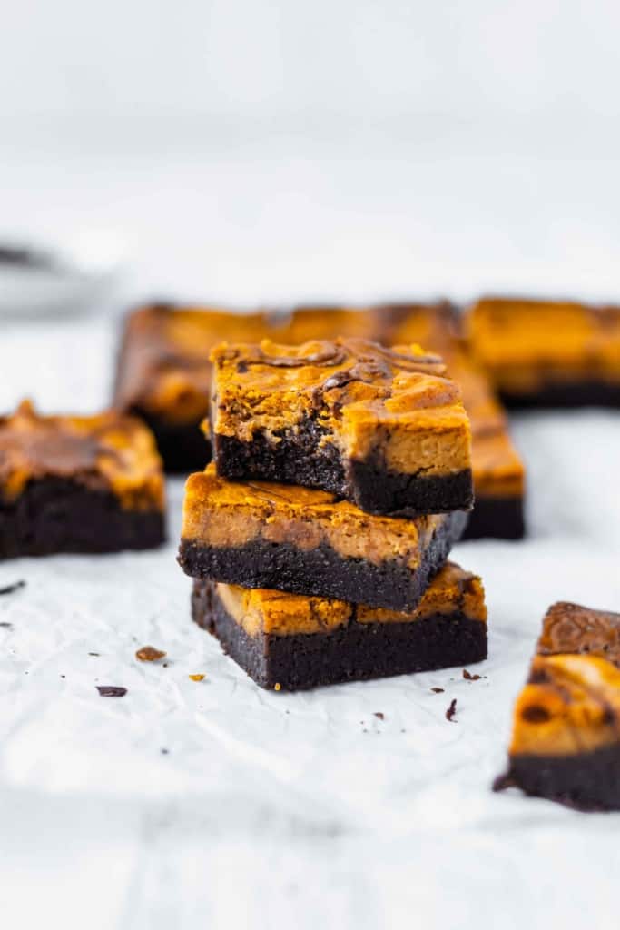 A stack of three pumpkin cheesecake brownies with more brownies scattered around.