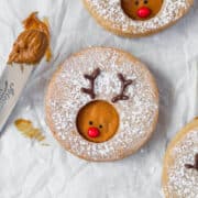 A reindeer cookie on a white surface next to a spatula with some cookie butter.