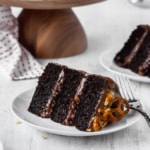 A slice of moist and fluffy chocolate cake with peanuts, pretzels, and chocolate buttercream frosting