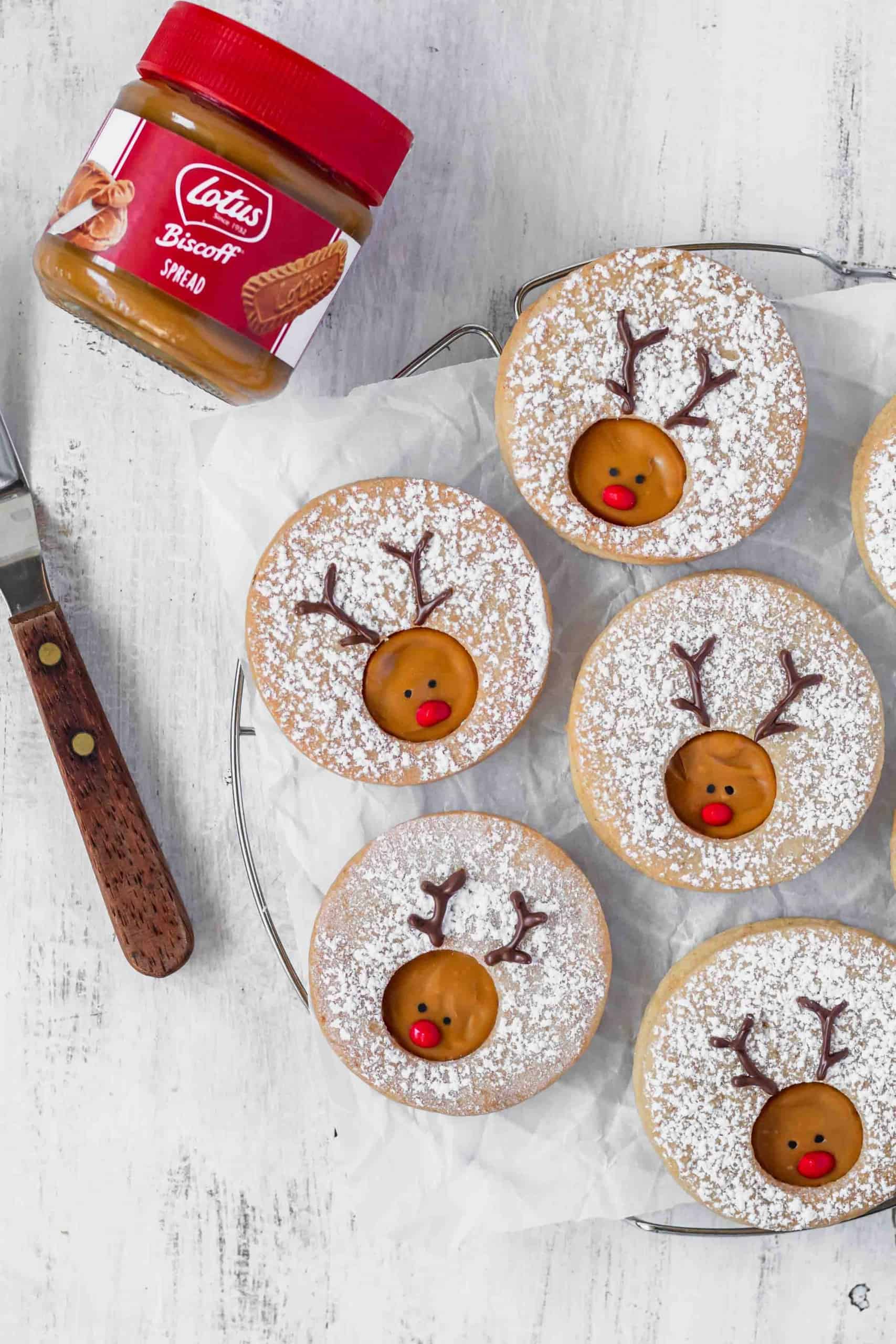 Reindeer cookies laying on a piece of parchment paper next to a jar of Biscoff spread.