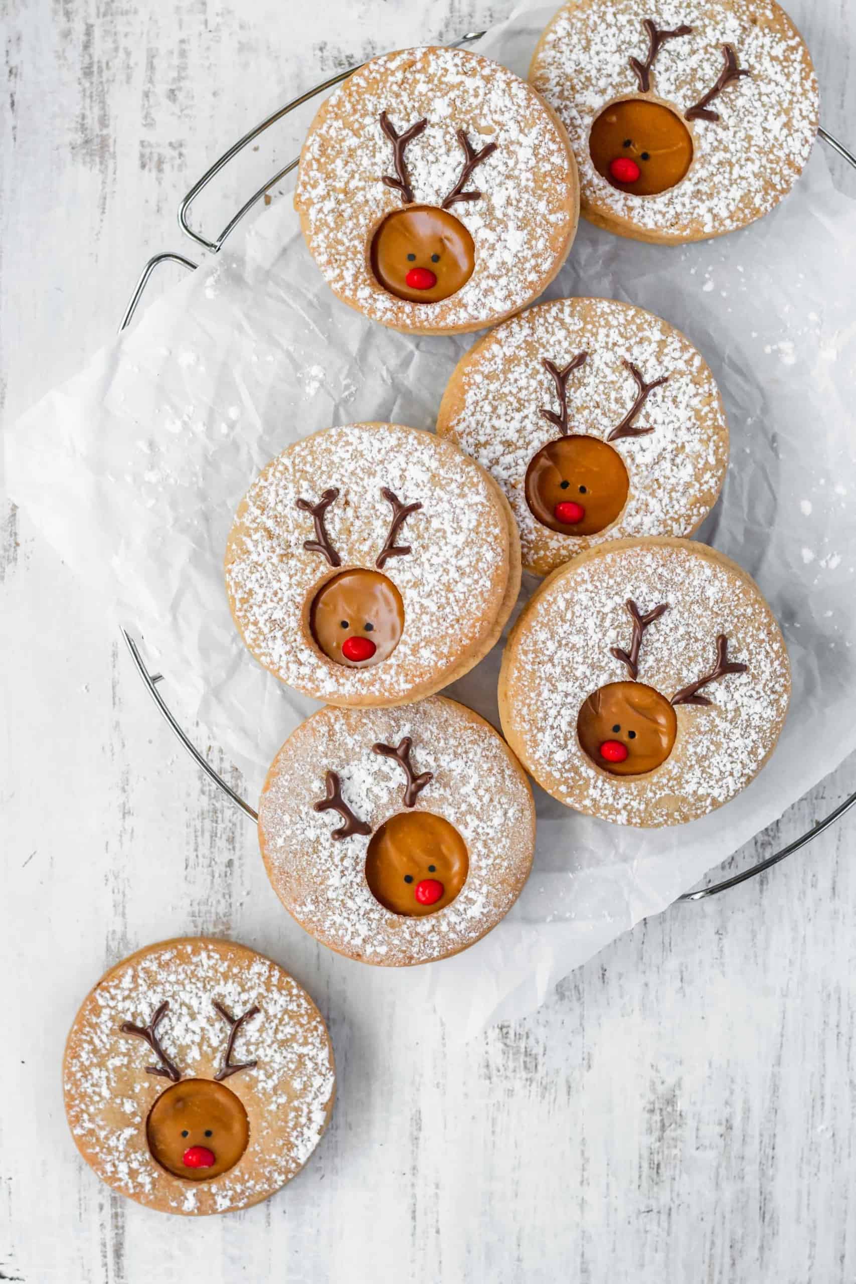 Reindeer cookies on a wire rack with one on the white surface underneath.