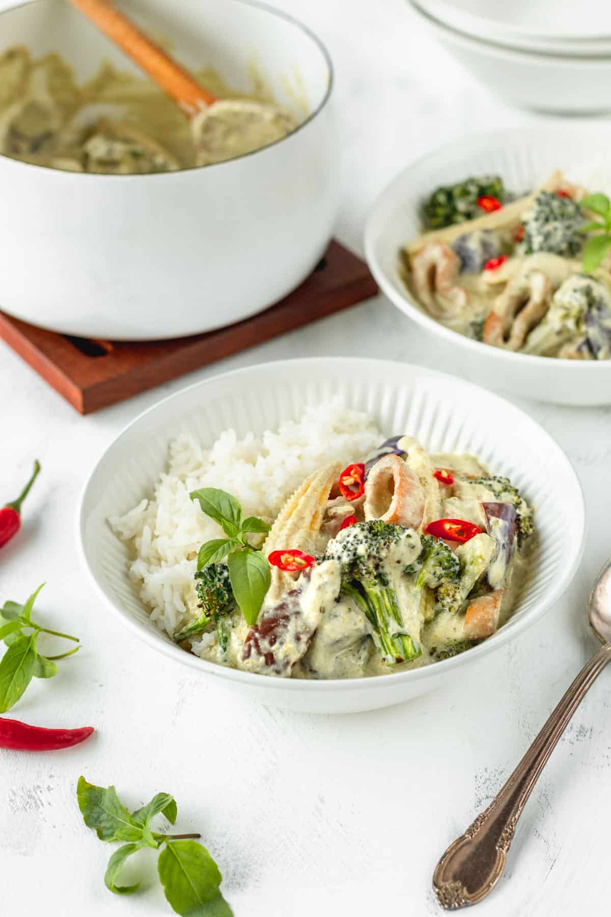 Vegan Thai green curry in a white bowl with another bowl and a white saucepan in the background.
