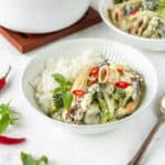 Square image of vegan Thai green curry in a white bowl with a silver spoon next to it.
