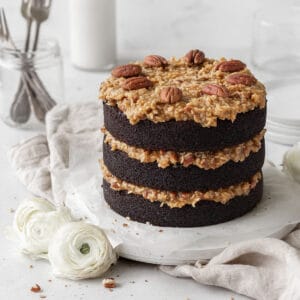 Gluten-free German chocolate cake on a round white board on a neutral linen.