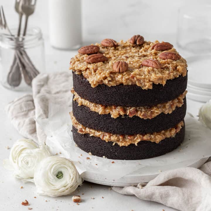 Gluten-free German chocolate cake on a round white board on a neutral linen.