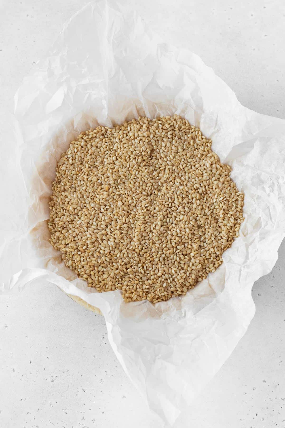 A crinkled piece of parchment paper fitted on top of the pie dough and filled with dry brown rice.