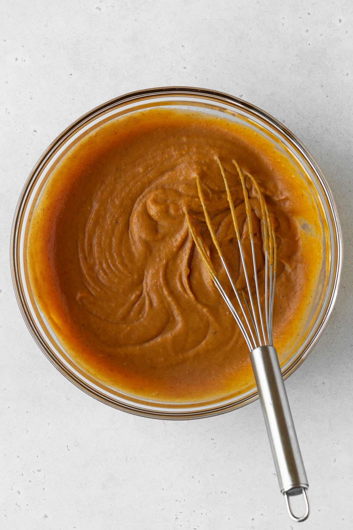 Pumpkin pie filling ingredients mixed together in a bowl with a whisk.