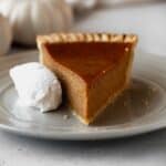 A slice of dairy-free pumpkin pie on a grey plate with a whipped coconut cream on the side.