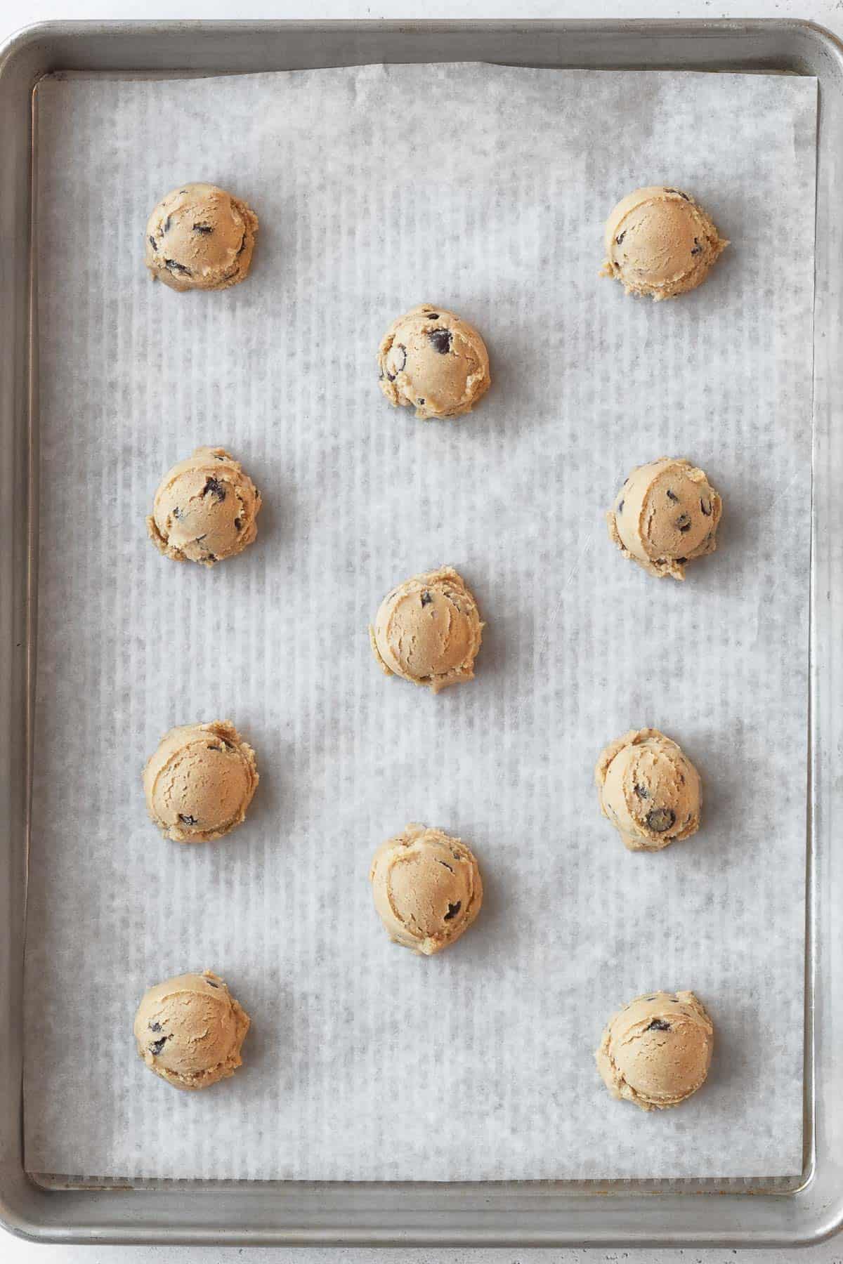 balls of chocolate chip cookie dough on a parchment lined baking sheet.