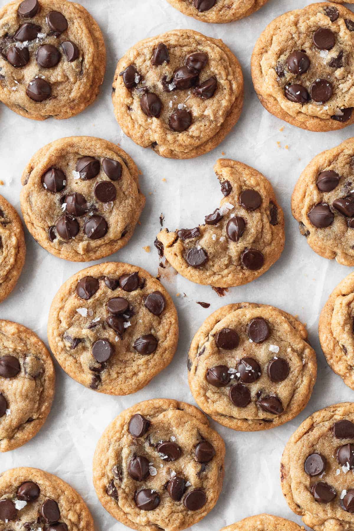 A bunch of gluten-free and dairy-free chocolate chip cookies on a piece of parchment with one in the middle that has a bite taken out.