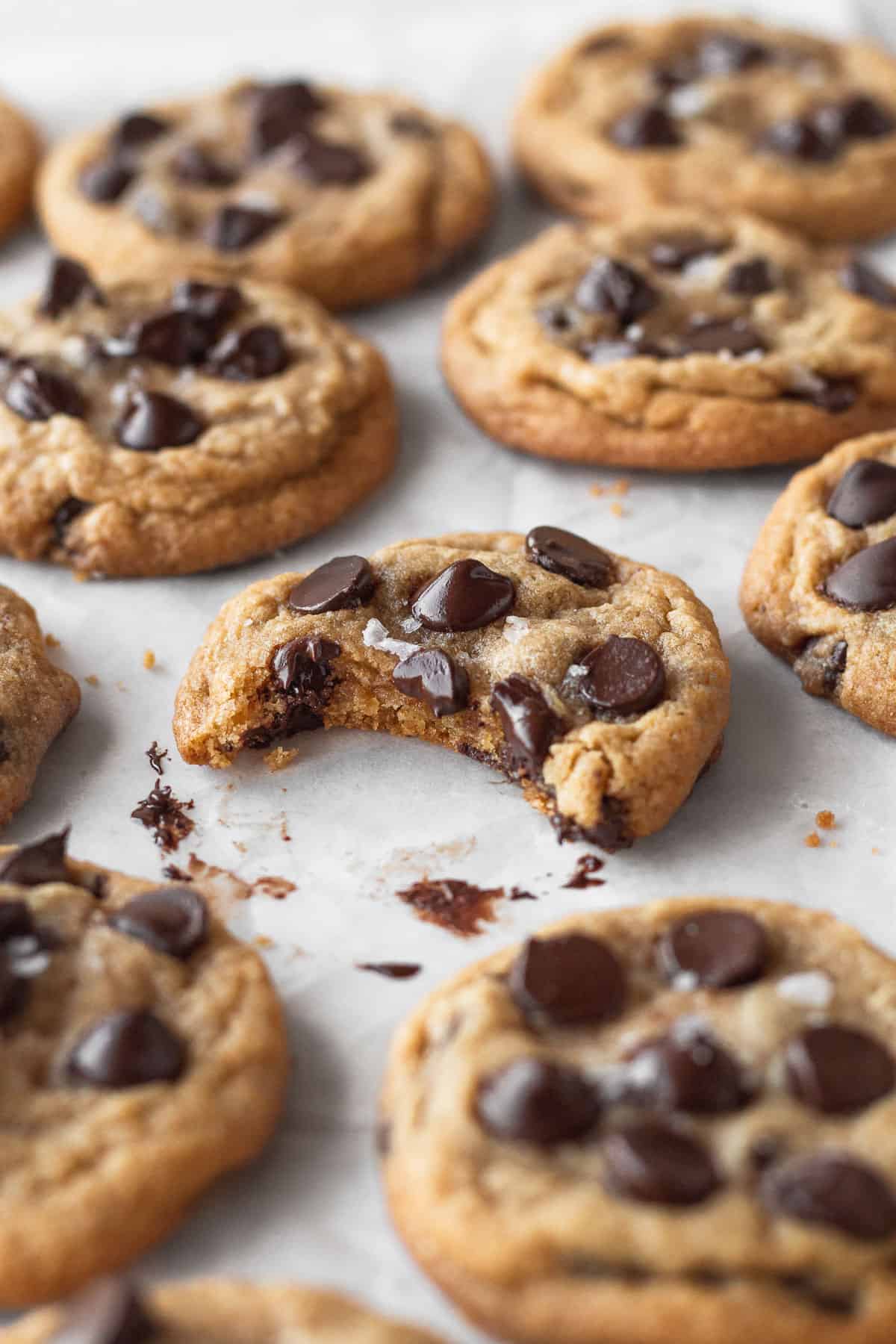 45 degree angle shot of gluten-free dairy free cookies with the one in focus with a bite taken out and melty chocolate on the parchment paper underneath.