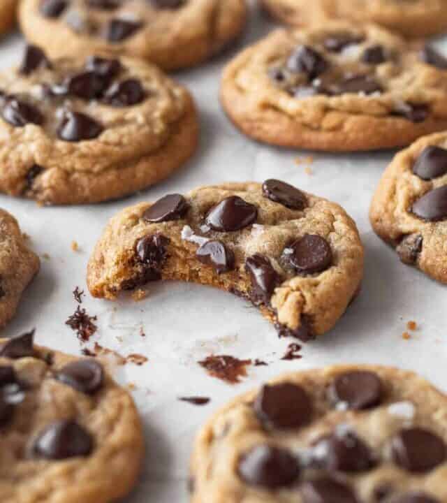 45 degree angle shot of gluten-free dairy free cookies with the one in focus with a bite taken out and melty chocolate on the parchment paper underneath.