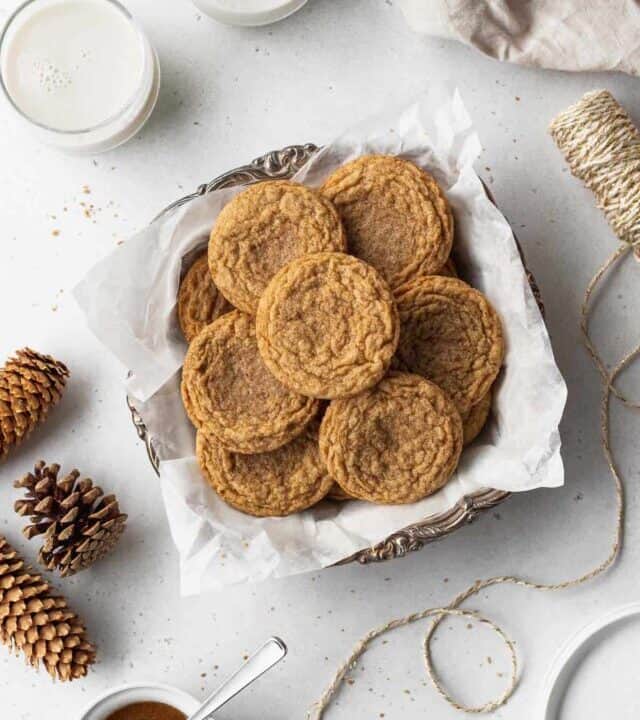 A platter of gluten free ginger snaps surrounded by glasses of milk, pine cones, string, and a dish of maple glaze icing.