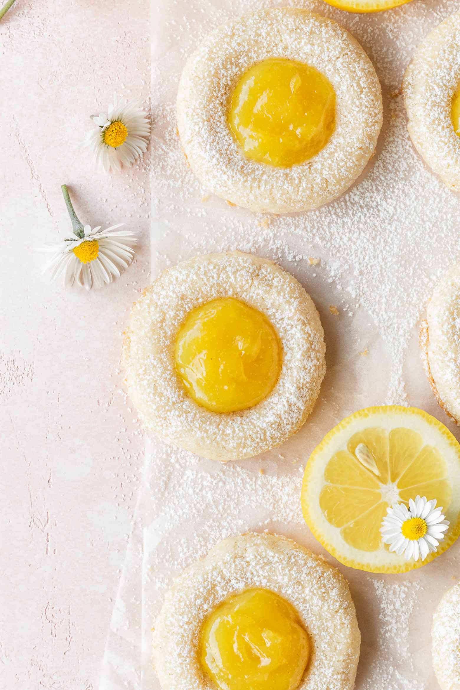 Lemon curd cookies on a pink surface with small white flowers scattered around.