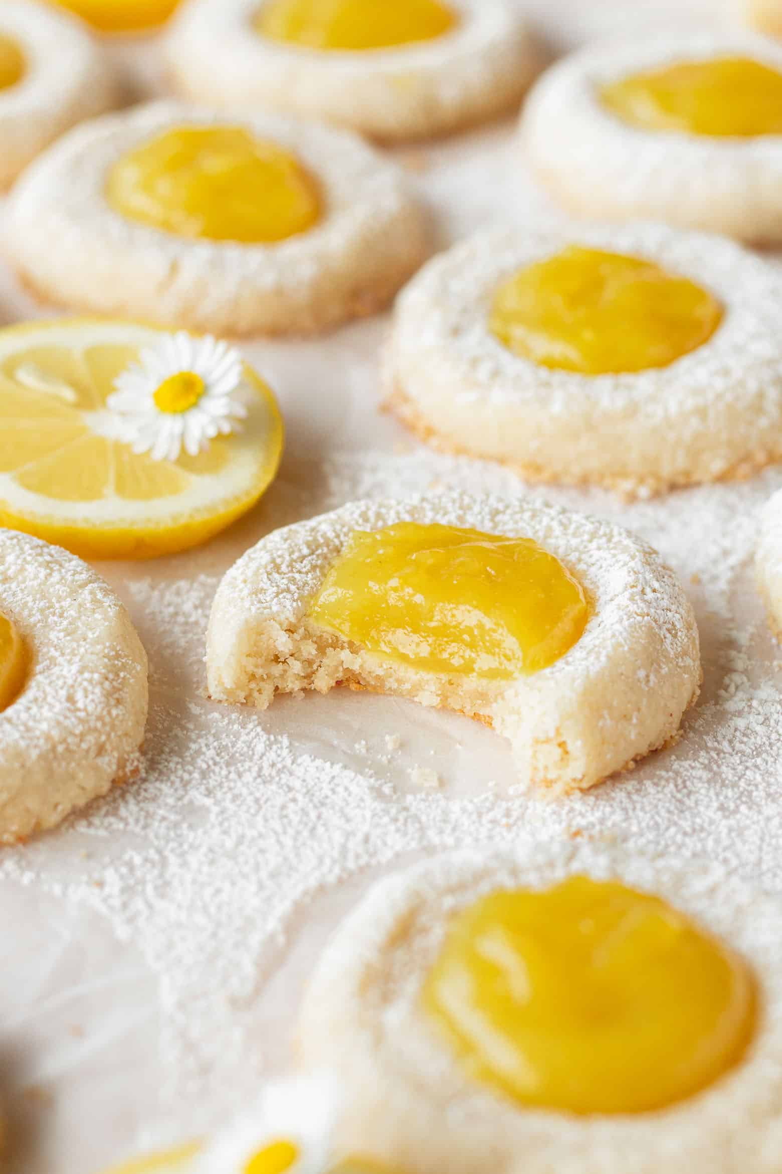 A bitten lemon thumbprint cookie with many cookies scattered around.