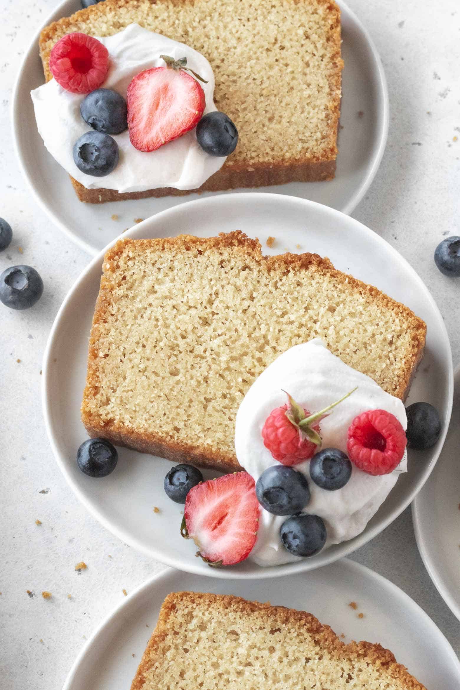 A slice of gluten-free pound cake on a plate with whipped cream and berries.