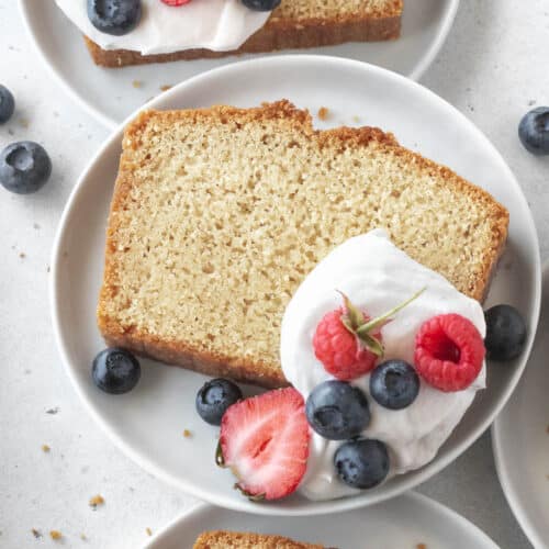 A slice of gluten-free pound cake on a plate with whipped cream and berries.